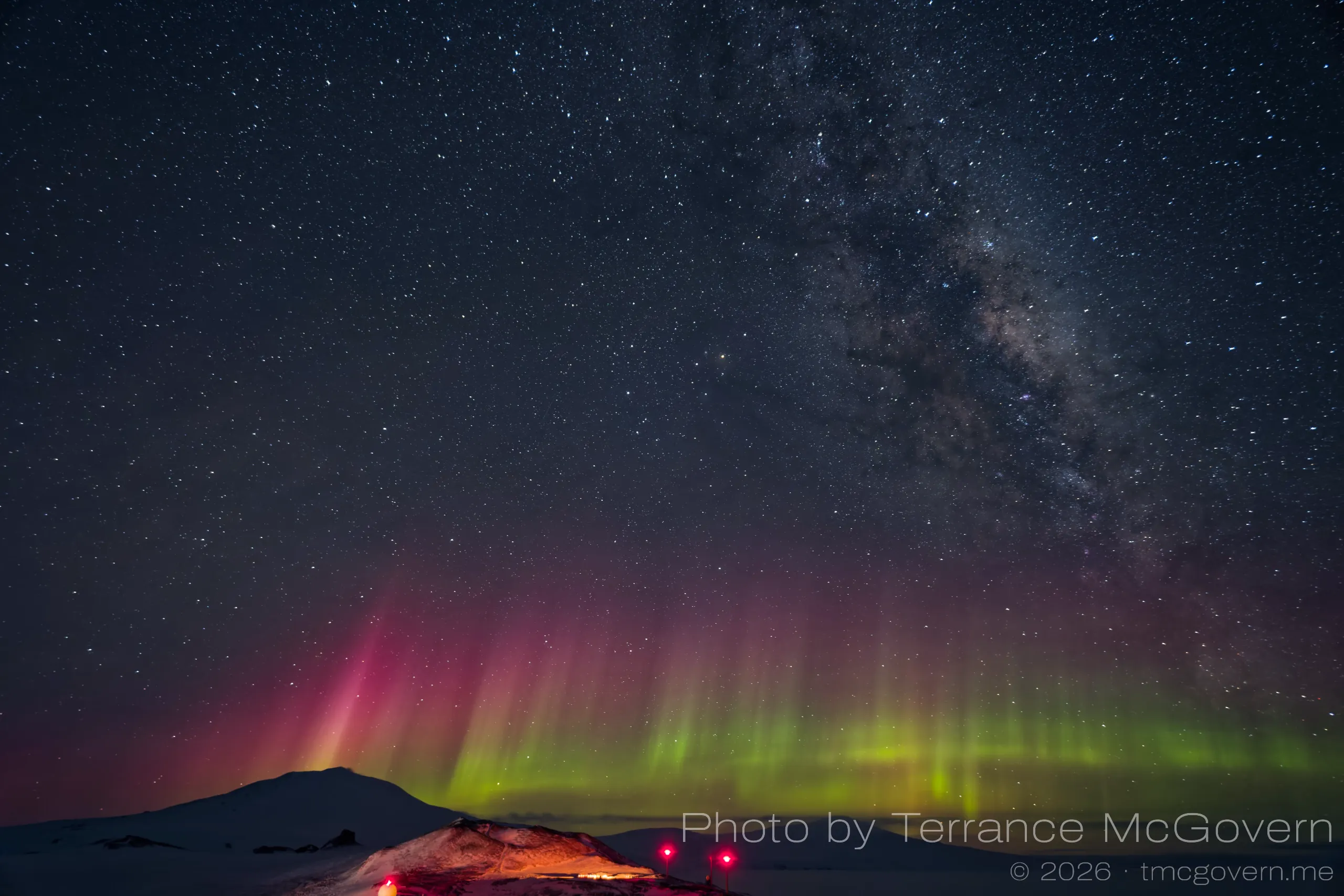 Auroras on the horizon under the milky way with the silhouette of Mt. Erebus in the background